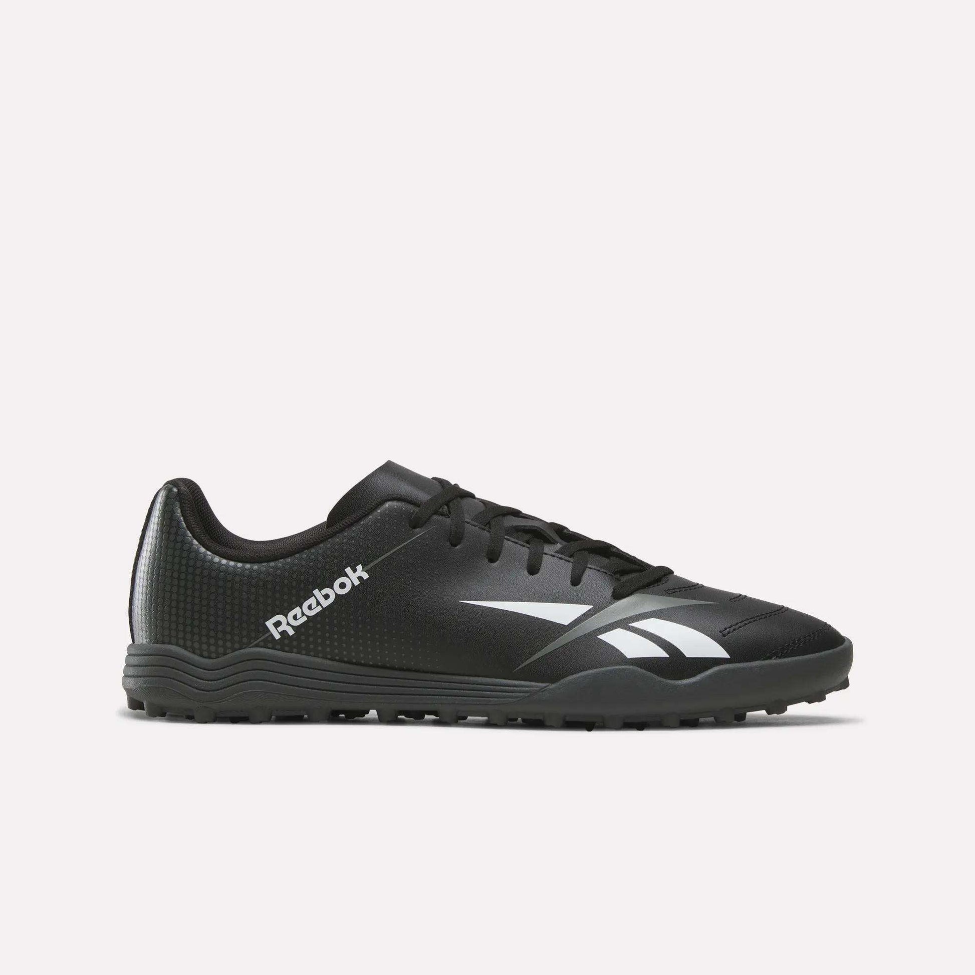 The Reebok Strike Turf Soccer Shoes in Black/White, featuring a white logo and accents, are designed for turf sports and perfect for soccer practice. Shown here is a side profile view on a plain white background.