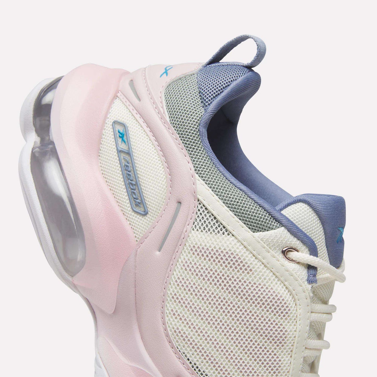 A close-up of the Reebok Women's DMX Series 3000 Training Shoes in white, highlighted with light pink and blue accents, showcases a mesh upper, blue laces, and a visible air cushion in the heel—demonstrating Reebok’s innovative DMX 3 Technology that distinguishes these shoes as among the best cushioned options for all-day comfort.