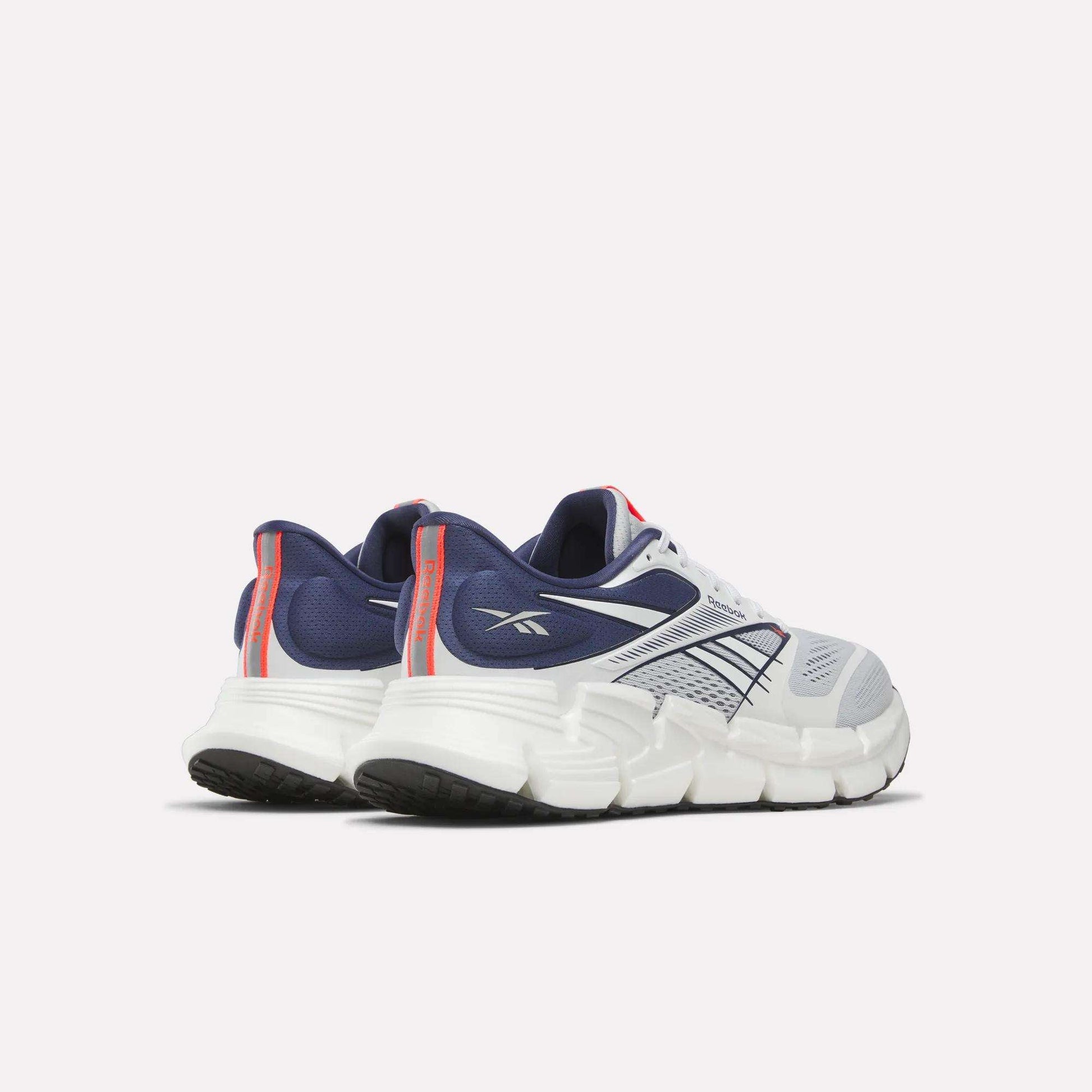 The Reebok Men's FloatZig 2 Running Shoes in white and navy, with red accents, are shown from a rear side view and feature chunky soles, mesh uppers, and Superfloat+ cushioning for added comfort.