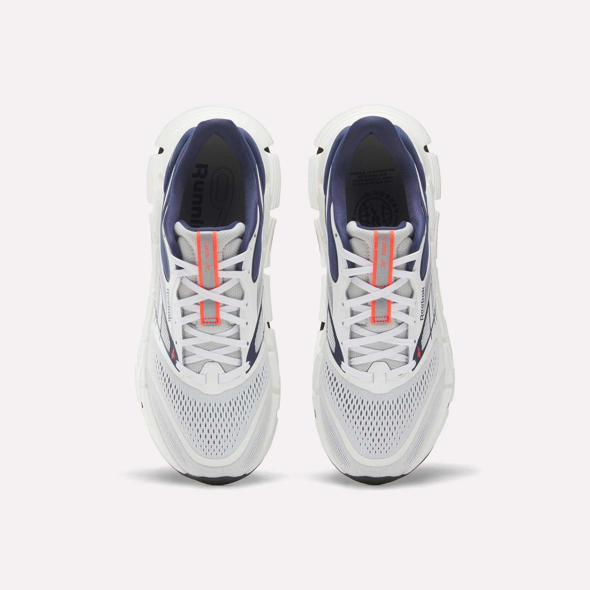 Top view of a pair of Reebok Men's FloatZig 2 Running Shoes with white mesh toes, navy interiors, Superfloat+ cushioning, and orange tongue branding, displayed side by side on a plain white background.