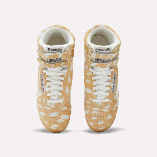 Top view of Women's Freestyle Hi Shoes by Reebok, featuring a classic 80s high-top design with a tan and white spotted fur-like pattern, white laces, and signature Reebok branding on the tongue and side.