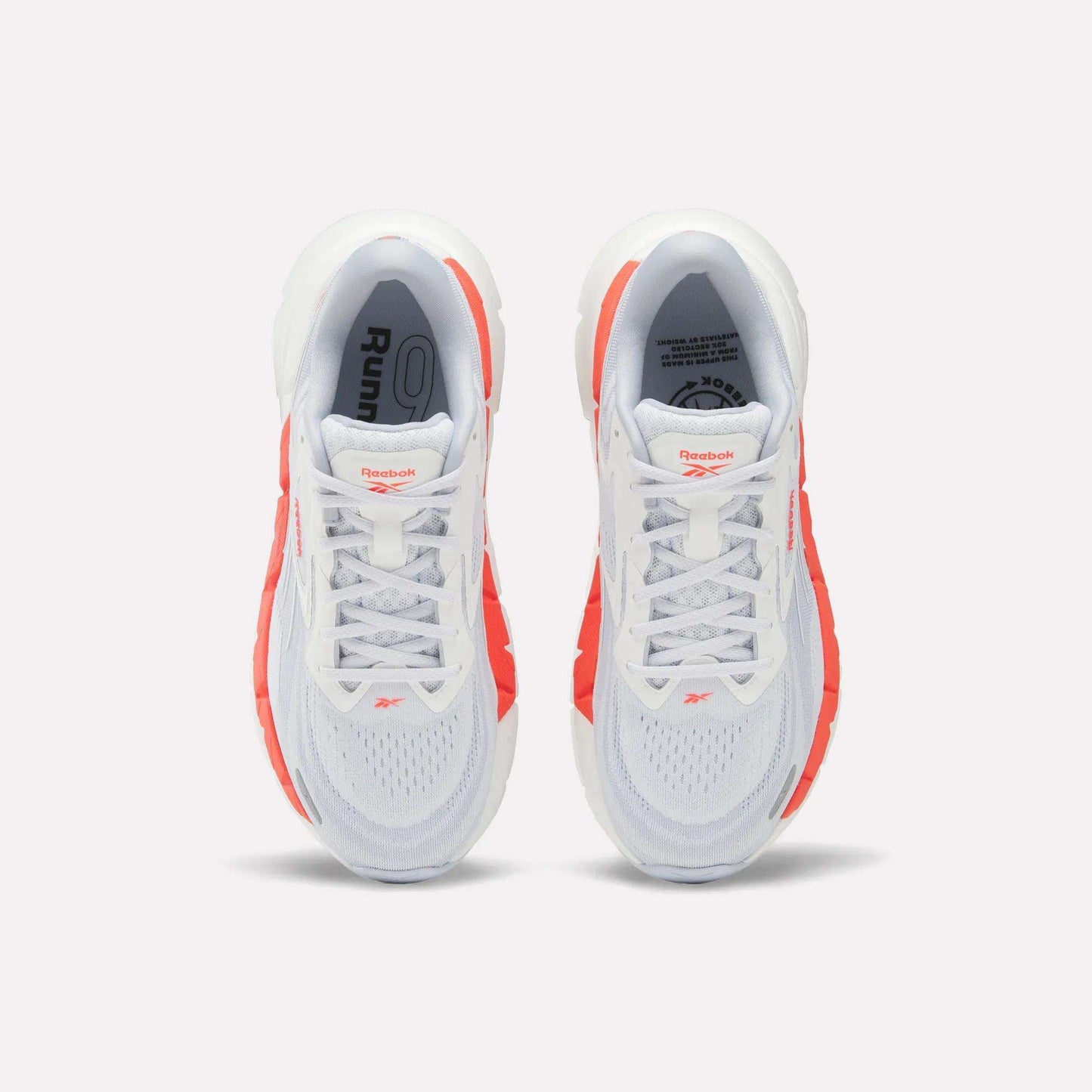 Top view of Women's FloatZig Double Running Shoes by Reebok, in white with bright orange side accents and branded tongue, set against a plain light background.