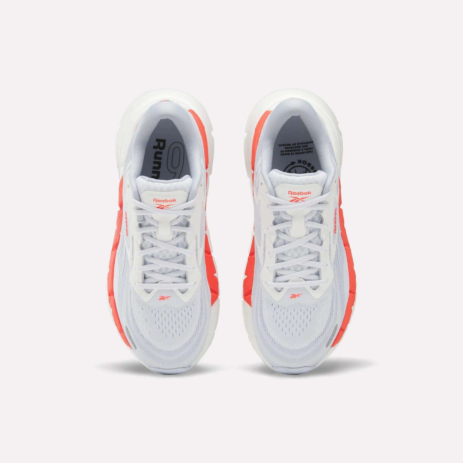 Top view of Women's FloatZig Double Running Shoes by Reebok, in white with bright orange side accents and branded tongue, set against a plain light background.