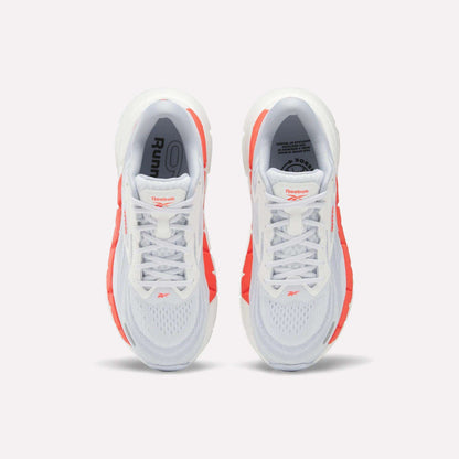 Top view of Women's FloatZig Double Running Shoes by Reebok, in white with bright orange side accents and branded tongue, set against a plain light background.