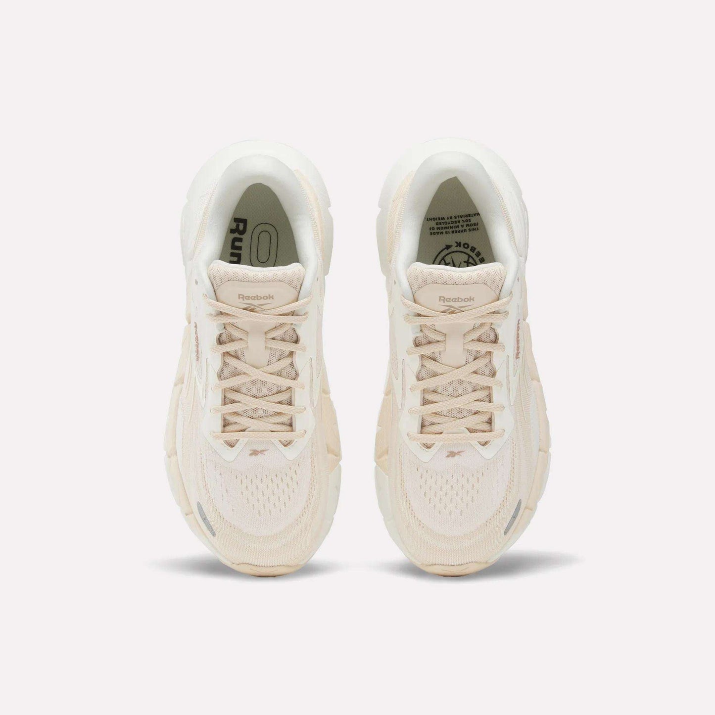 A pair of Women's FloatZig Double Running Shoes by Reebok in beige are shown from above, featuring laces, mesh texture, and logo details on the tongues—designed for max-cushioned runs—set against a plain white background.
