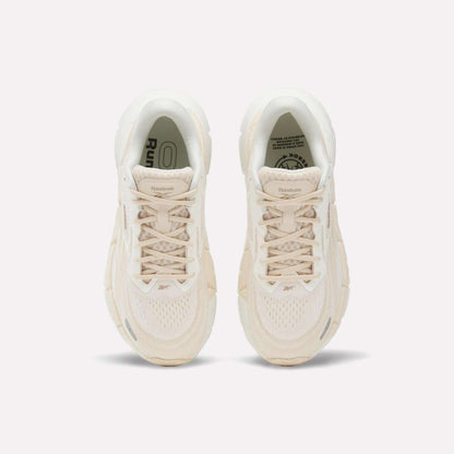 A pair of Women's FloatZig Double Running Shoes by Reebok in beige are shown from above, featuring laces, mesh texture, and logo details on the tongues—designed for max-cushioned runs—set against a plain white background.
