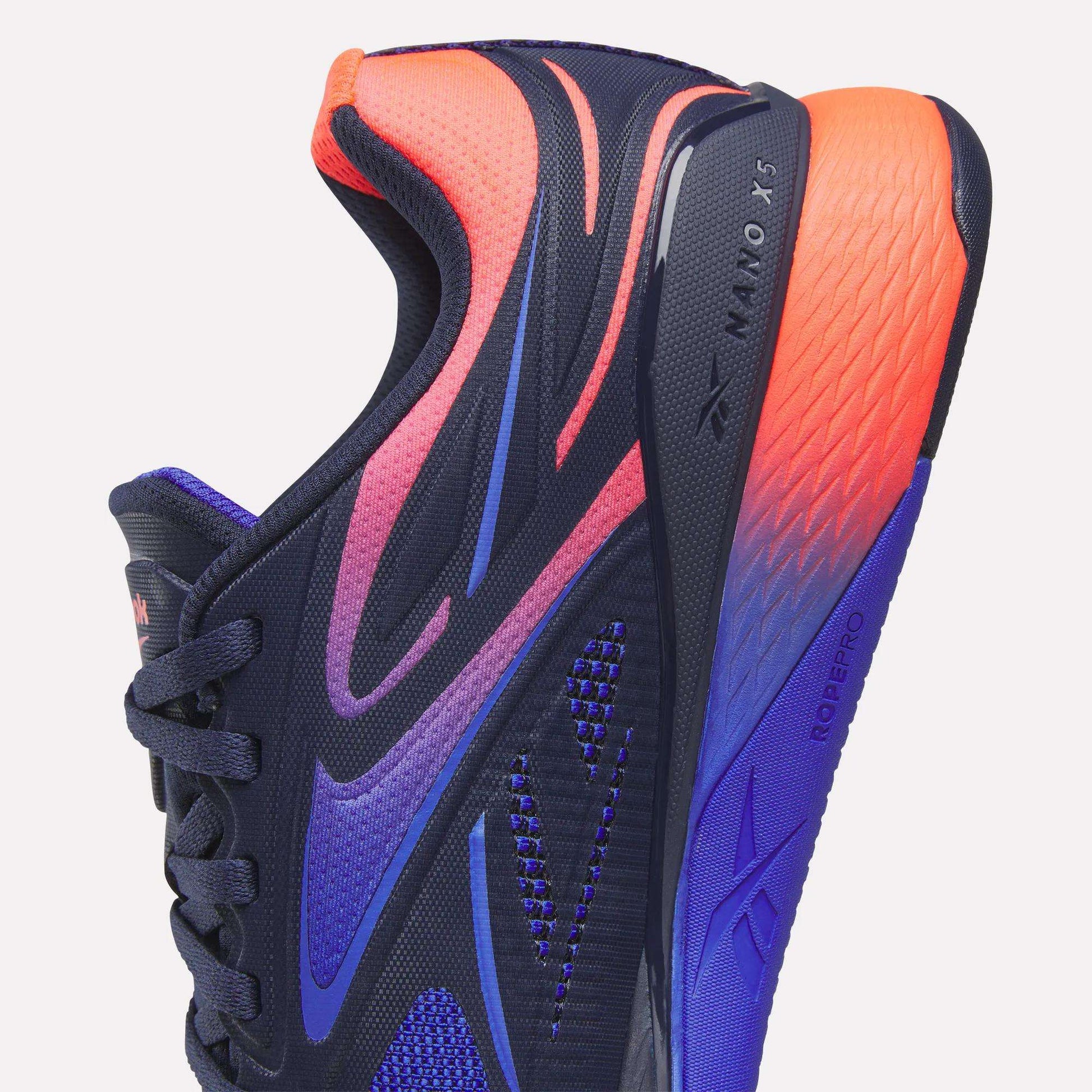 Close-up of Reebok Nano X5 Edge Training Shoes in navy blue with bold purple, pink, and orange gradients. Features textured mesh, black laces, and “Nano X5 Edge” with “RopePro” visible on the side and sole for superior performance.