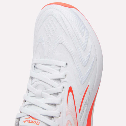 Close-up of the Reebok Women's Nano X5 Edge Training Shoes in white with orange accents, showcasing a wavy-patterned upper, white laces, and a partially visible logo near the toe. Perfect addition to any women’s HIIT shoe collection.