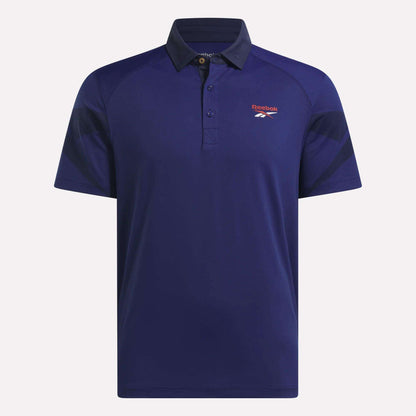 The Reebok Men's Signature Vector Colorblocked Polo Shirt is a dark blue, short-sleeve golf polo with black sleeve accents, a button-up collar, UPF 30+ sun protection, and moisture-wicking fabric. Red and white Reebok logo on the left chest.