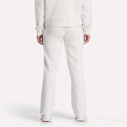 A person is seen from behind, showing only lower back and legs, wearing Reebok Women's Cozy Classic Sweatpants in soft white cotton blend with a matching long-sleeve top and white shoes, set against a plain white background.