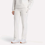A woman wears Reebok Women's Cozy Classic Sweatpants in off-white, paired with a matching sweatshirt and white sneakers, standing against a light background.