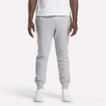 A person stands facing forward against a plain white background, wearing a white t-shirt, Reebok Men's Motion Joggers in a slim fit, and white sneakers.
