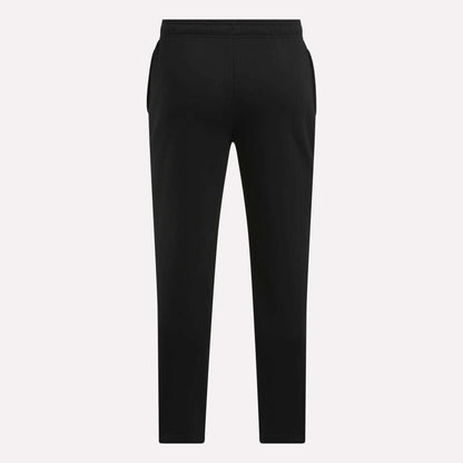 Men's Patent Pants by Reebok in black, featuring a slim fit, elastic waistband, and tapered legs, shown from the back against a plain light background.