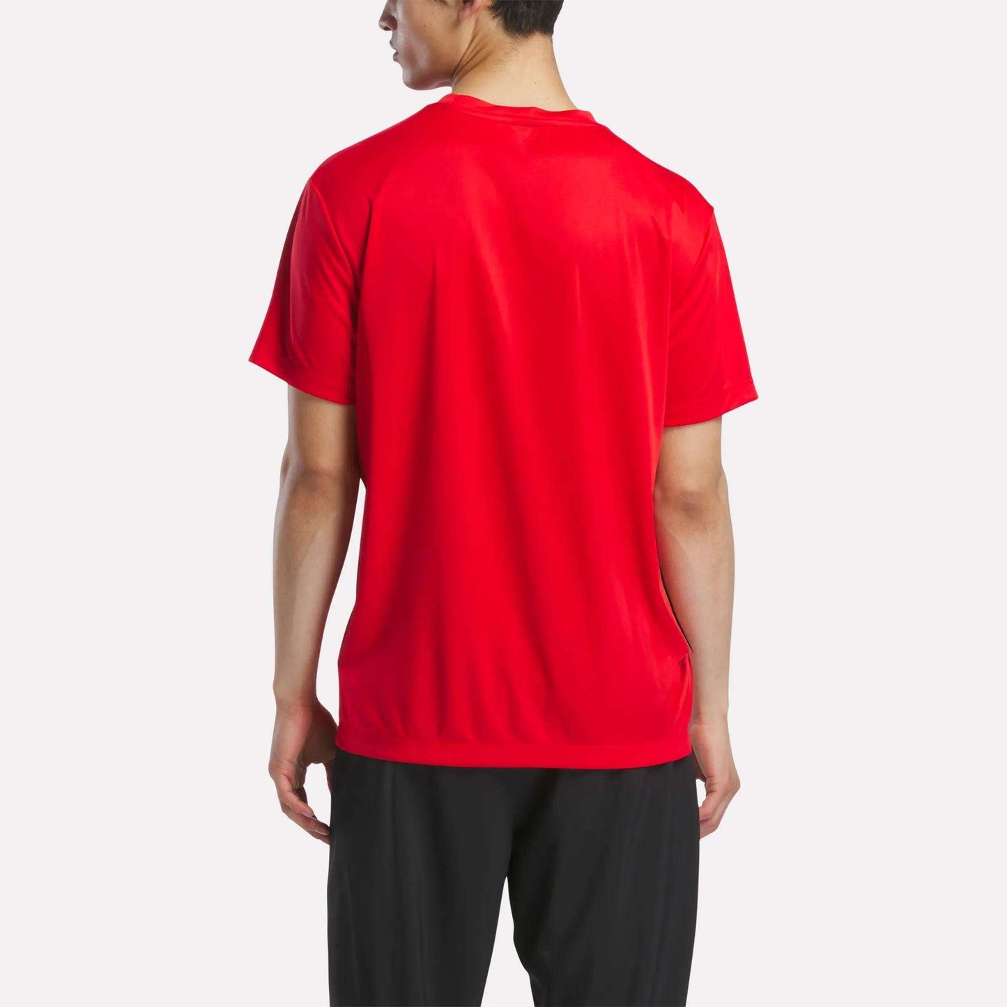 A man is shown from the back wearing a Men's Short Sleeve Tech Training T-Shirt by Reebok in red and black pants, standing against a plain white background.