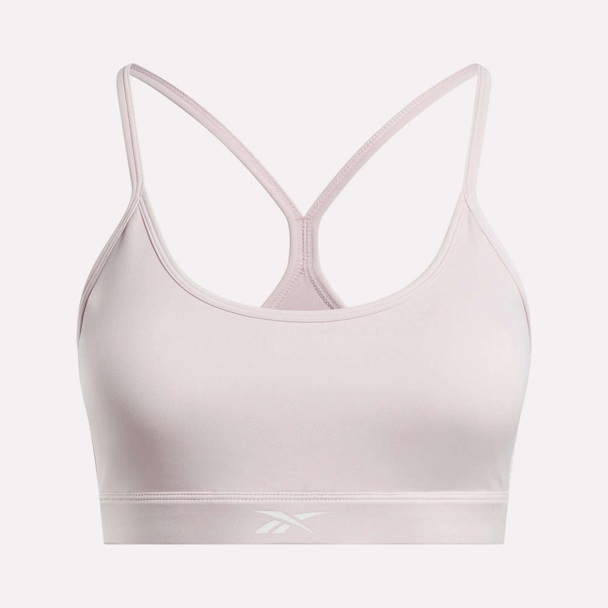 The Women's Strappy Sports Bra by Reebok features a light pink color, thin racerback straps, and a subtle front logo on the band. Made from smooth, stretchy quick-drying fabric, it delivers comfort and support for medium-impact workouts.