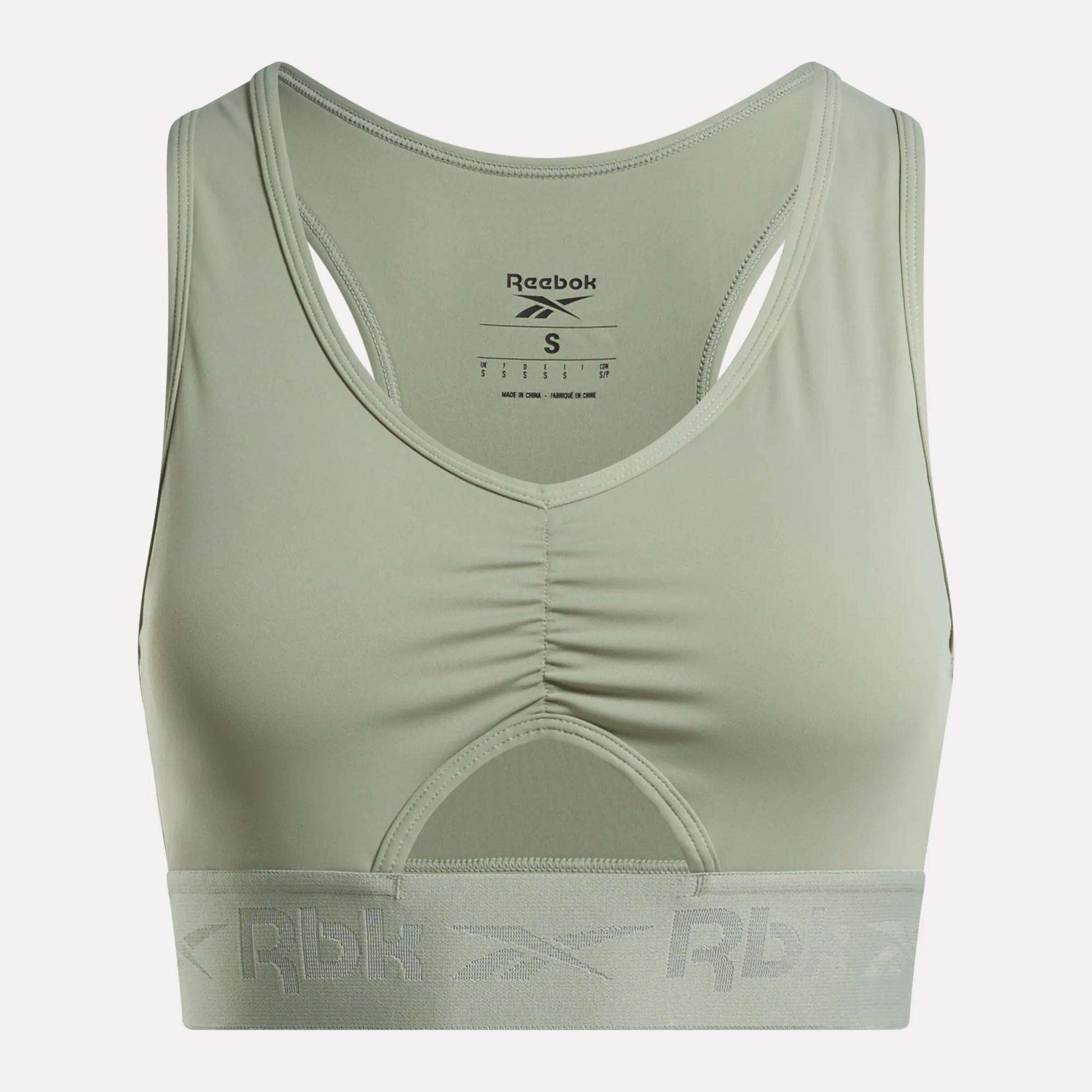 The Women's Ruched Sports Bra by Reebok comes in light green and features a racerback design with a ruched front. Designed for medium-impact activities, it includes performance technology for added comfort, a wide elastic band at the bottom with the Rbk logo, and a visible inner label at the back.