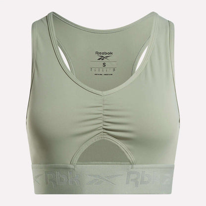 The Women's Ruched Sports Bra by Reebok comes in light green and features a racerback design with a ruched front. Designed for medium-impact activities, it includes performance technology for added comfort, a wide elastic band at the bottom with the Rbk logo, and a visible inner label at the back.