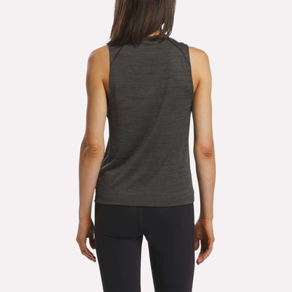A woman with long brown hair is seen from behind, wearing a sleeveless Reebok Women's Training Tank Top in dark gray paired with black leggings, standing against a plain white background.