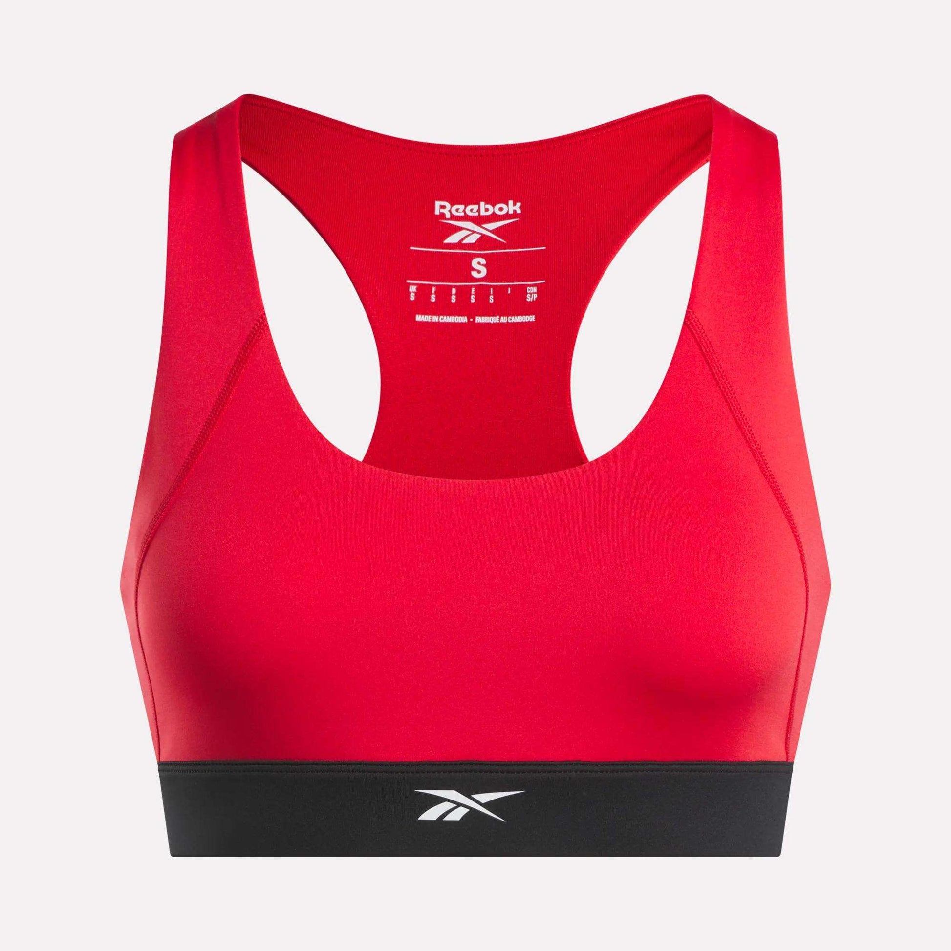 A red Reebok Women's Racer Sports Bra featuring a supportive racerback design, contrasting black band at the bottom, and mid-impact support. The Reebok logo appears on the inner back and front band, making it an ideal choice for reliable workout performance.