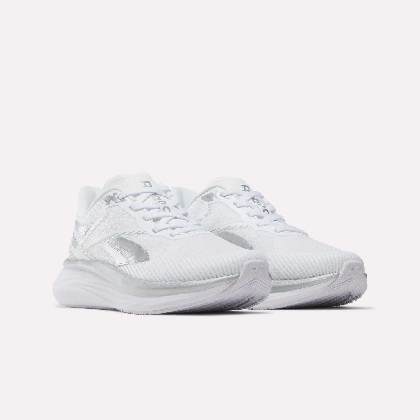 A pair of Women’s Viva Speed Shoes by Reebok in white with silver accents, featuring breathable mesh uppers, a cushioned midsole for enhanced support, thick cushioned soles, and a secure lace-up closure—all showcased against a plain white background.