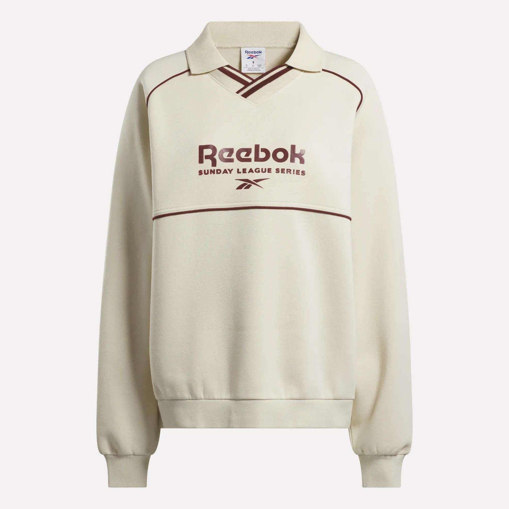 The Reebok Women's Heritage Crewneck Sweatshirt features a cream brushback fleece, collar, maroon piping, Sunday League Series text and logo on the front, plus long sleeves with ribbed cuffs and hem.
