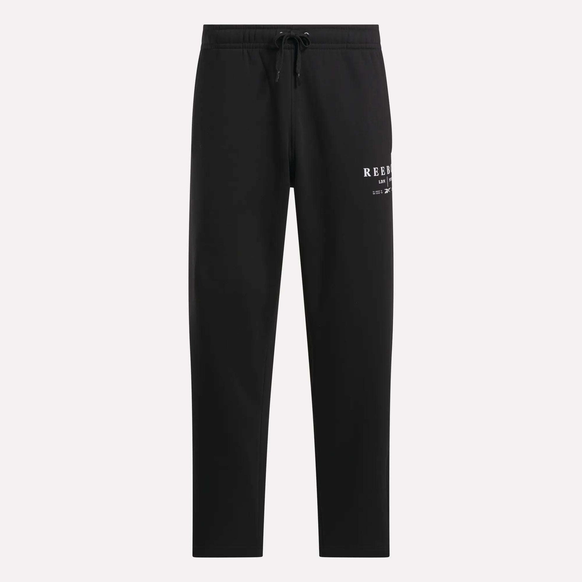 Men's International Straight Leg Pants by Reebok in black plush fleece, designed in a relaxed jogger style with a drawstring waist and straight legs. A small white Reebok logo appears on the upper left thigh, and the open hem pants are displayed against a plain light gray background.