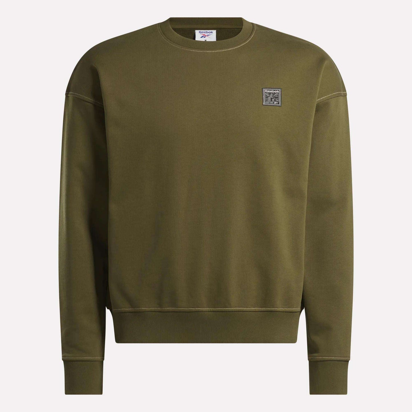 The Reebok Men's Patch Logo Crewneck Sweatshirt features a relaxed fit in olive green with long sleeves, ribbed cuffs and hem, crew neck, and a small square logo patch on the left chest. Displayed against a plain light background.