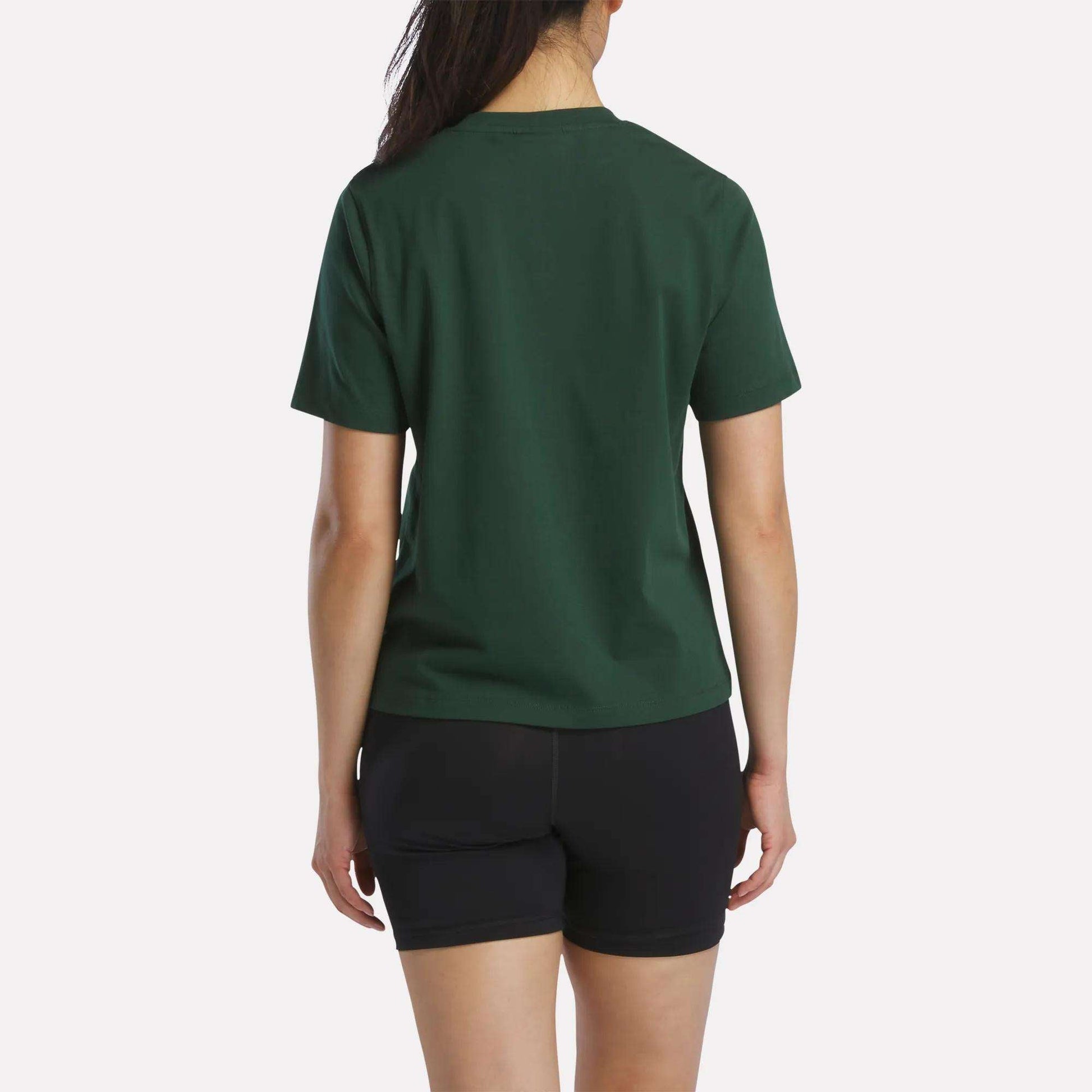 A person stands facing away, wearing a Women's Fitted Graphic T-Shirt by Reebok in dark green and black shorts, set against a plain light background.