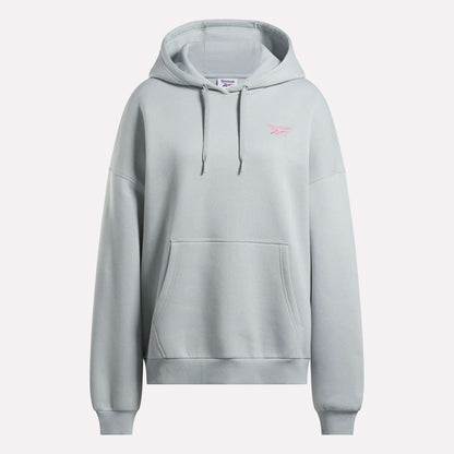 The Reebok Women's Relaxed Fleece Hoodie is an oversized light gray hoodie featuring a front pocket, drawstring hood, and a small pink Reebok logo on the left chest. It is shown against a plain white background.