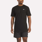 A man in a relaxed fit black Reebok Men's Identity Small Logo T-Shirt and matching shorts stands against a light background, facing slightly to the side.