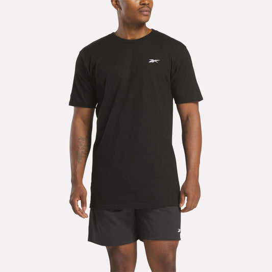 A man in a relaxed fit black Reebok Men's Identity Small Logo T-Shirt and matching shorts stands against a light background, facing slightly to the side.