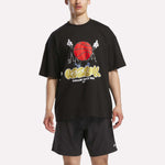 A man in a loose black Reebok Men's Basketball T-Shirt featuring a bold graphic and matching black shorts stands against a plain white background.