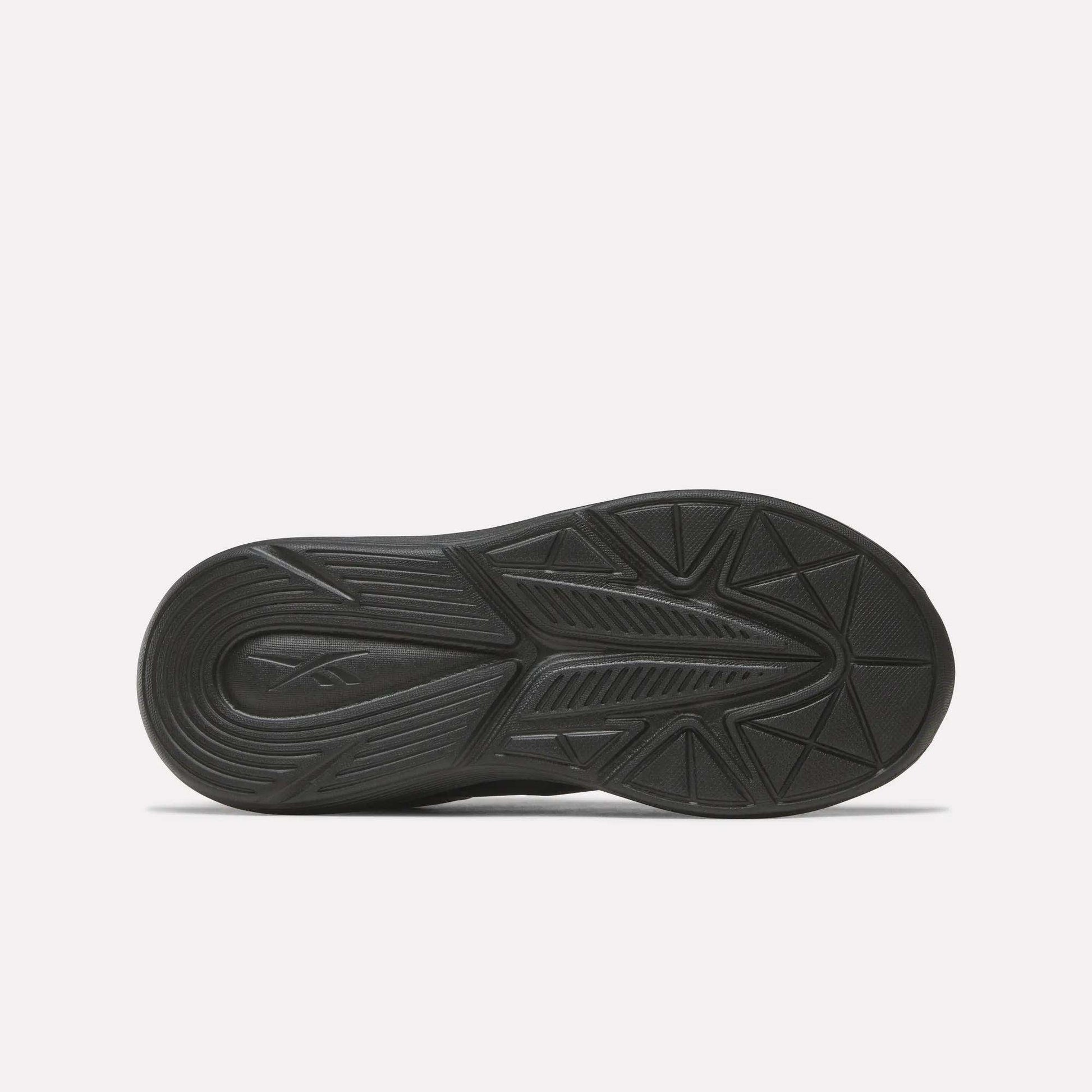 The image shows the black rubber outsole of Reebok Rush Runner 6.0 Elastic Lace Top Strap Running Shoes for little kids, featuring geometric tread patterns for traction and comfort, viewed from below against a plain white background.
