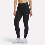 A person wearing Reebok Women's Speed HR High-Rise Leggings in black, featuring a small blue logo on the upper thigh, paired with white athletic shoes, stands against a plain light background.