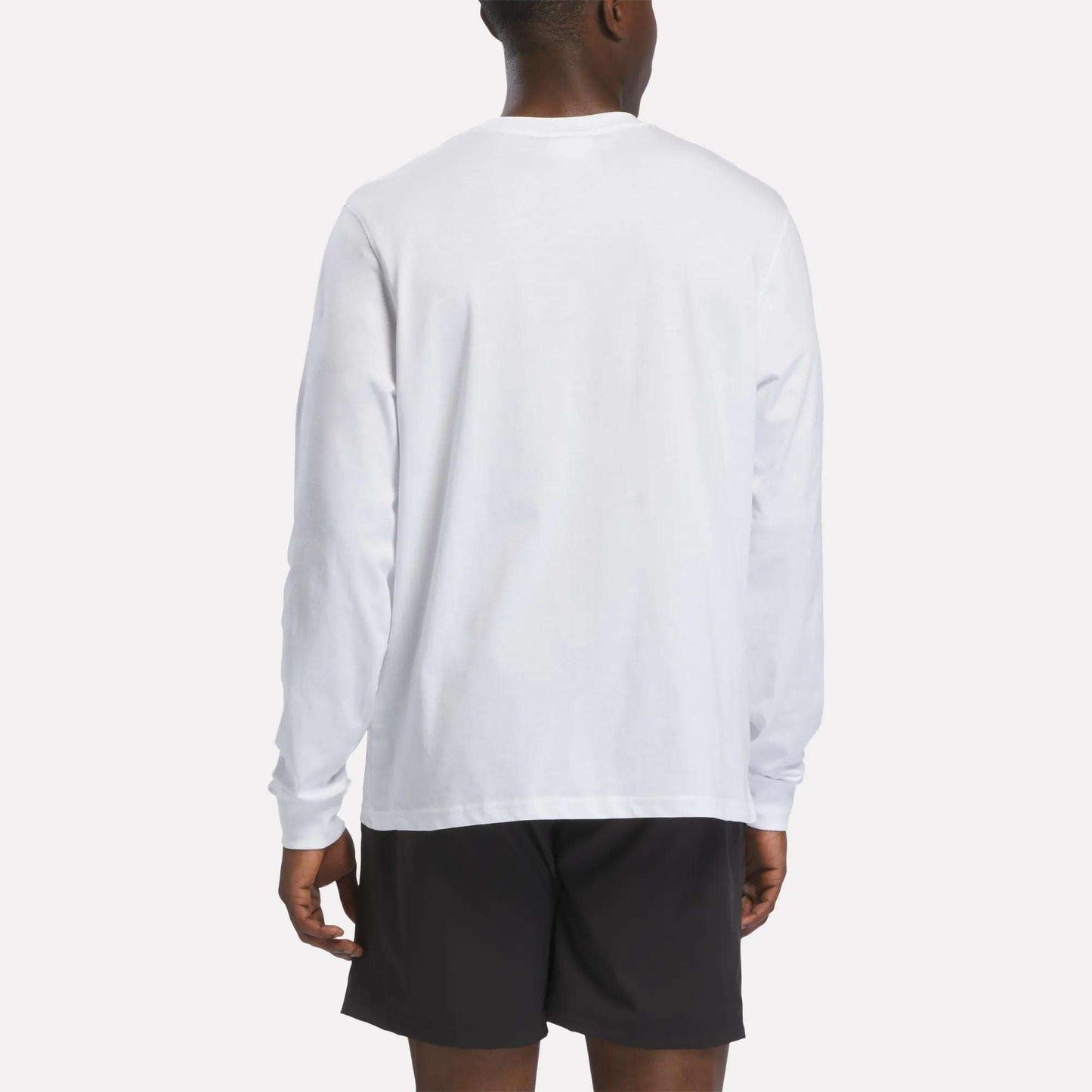 A person wearing a Reebok Men's Long Sleeve T-Shirt in white and black shorts is standing with their back to the camera against a plain background.