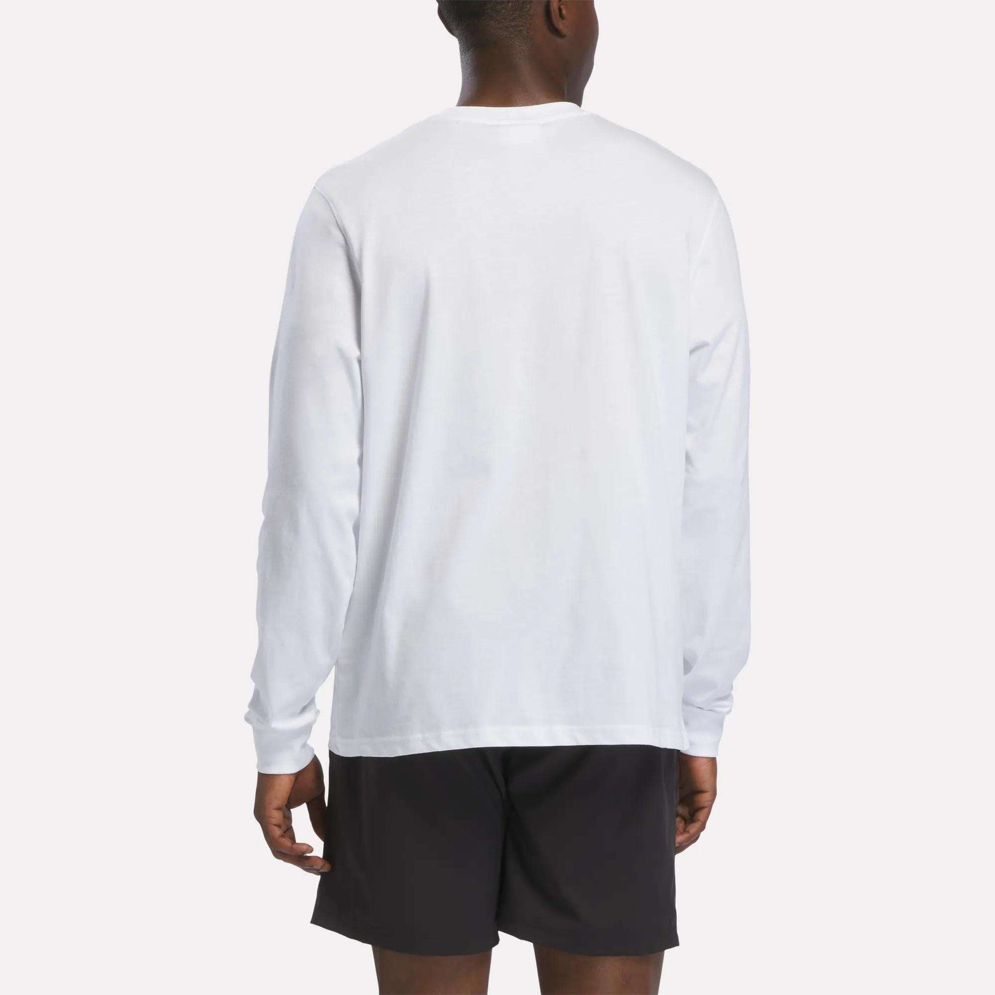 A person wearing a Reebok Men's Long Sleeve T-Shirt in white and black shorts is standing with their back to the camera against a plain background.