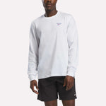 A person wearing a Reebok Men's Long Sleeve T-Shirt in white and black Reebok shorts stands against a plain, light background.