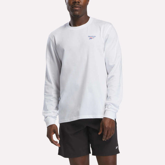 A person wearing a Reebok Men's Long Sleeve T-Shirt in white and black Reebok shorts stands against a plain, light background.