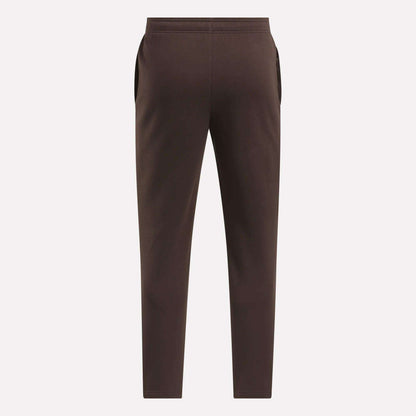 The Reebok Men's Patent Pants in brown are shown flat from the back on a light background, featuring an elastic waistband and side pockets. Made with a cotton-poly blend for comfort and durability.
