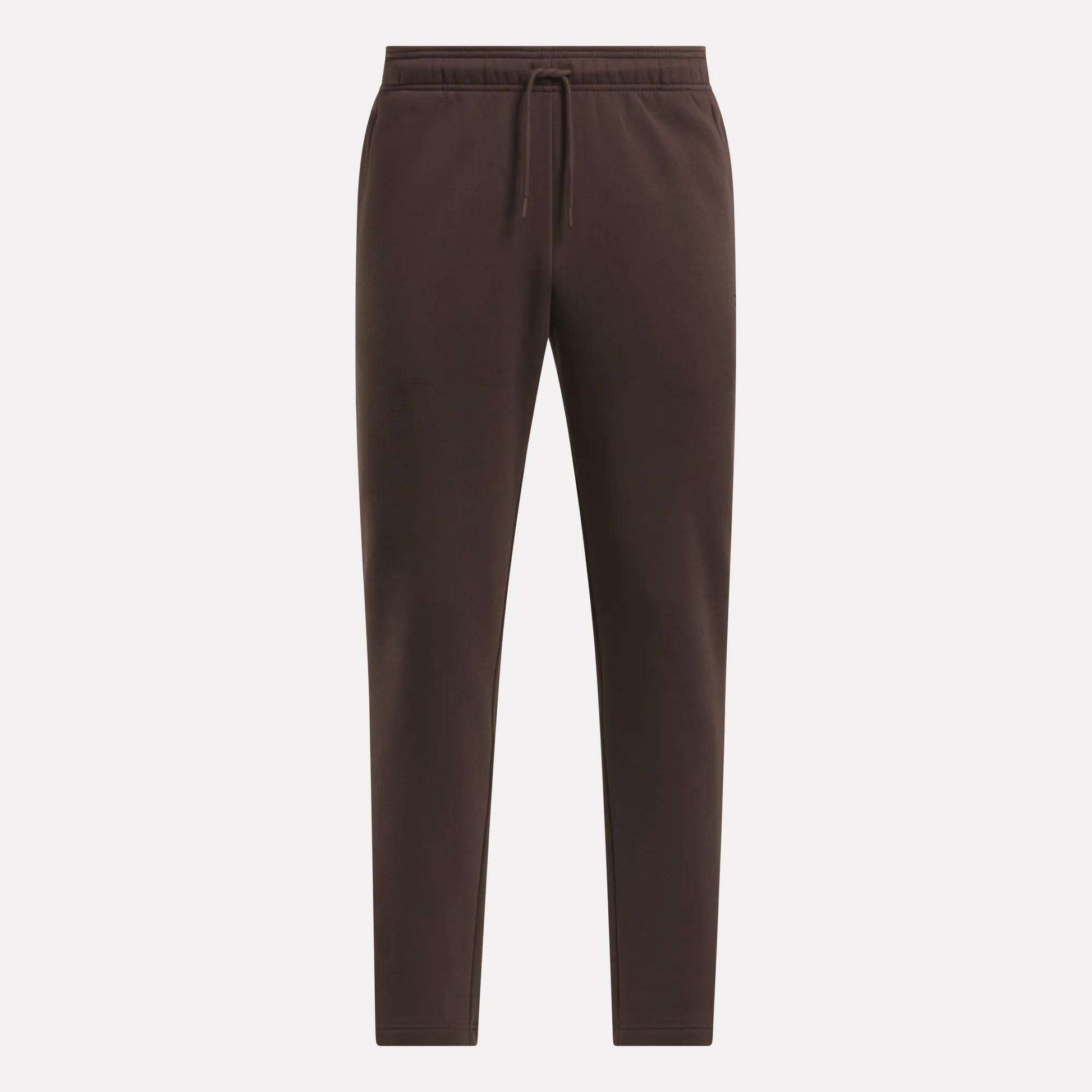 The Men's Patent Pants by Reebok are dark brown, slim fit joggers with an elastic waistband, drawstring, and tapered legs. Made from a soft cotton-poly blend, they are shown against a light background.