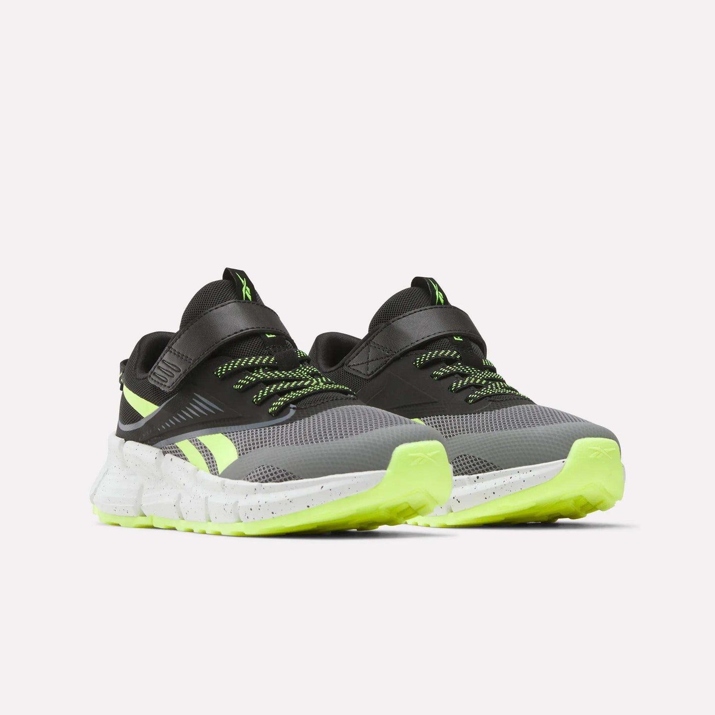 The Reebok Zig Dynamica 6 Running Shoes for little kids feature a black and gray design with neon green accents, green-tipped laces, and speckled white soles, displayed on a light background.