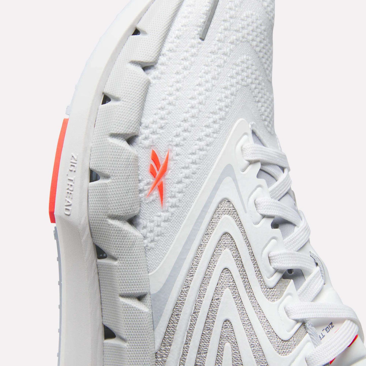 Close-up of Reebok Women's FloatZig Tread Running Shoe with breathable mesh, textured sole, gray curved patterns, white laces, and an orange logo. “Zig Kinetica” and “Zig” are embossed near the heel on the sole.