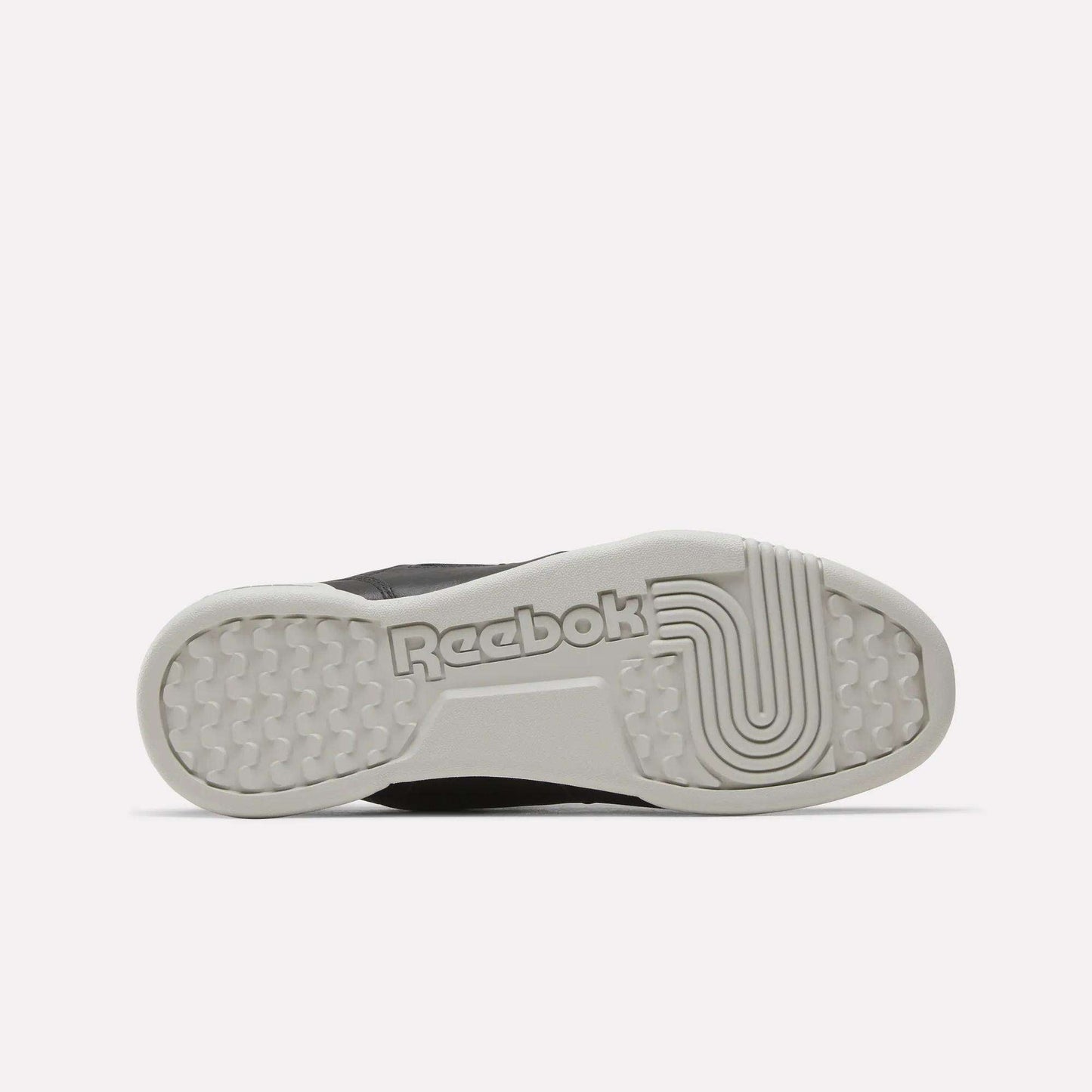 The image shows the sole of the Reebok Workout Plus Shoes in light gray, featuring the Reebok logo and a combination of textured and linear grip patterns.