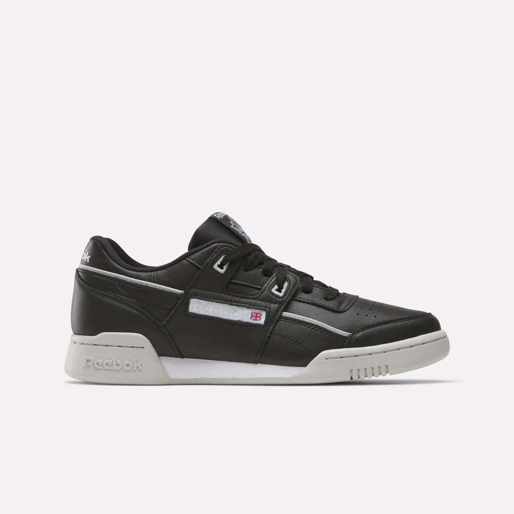 The Reebok Workout Plus Shoes are black leather low-tops with a white sole and subtle white and gray accents. Stylish for workouts, they display the Reebok logo and flag on the side.