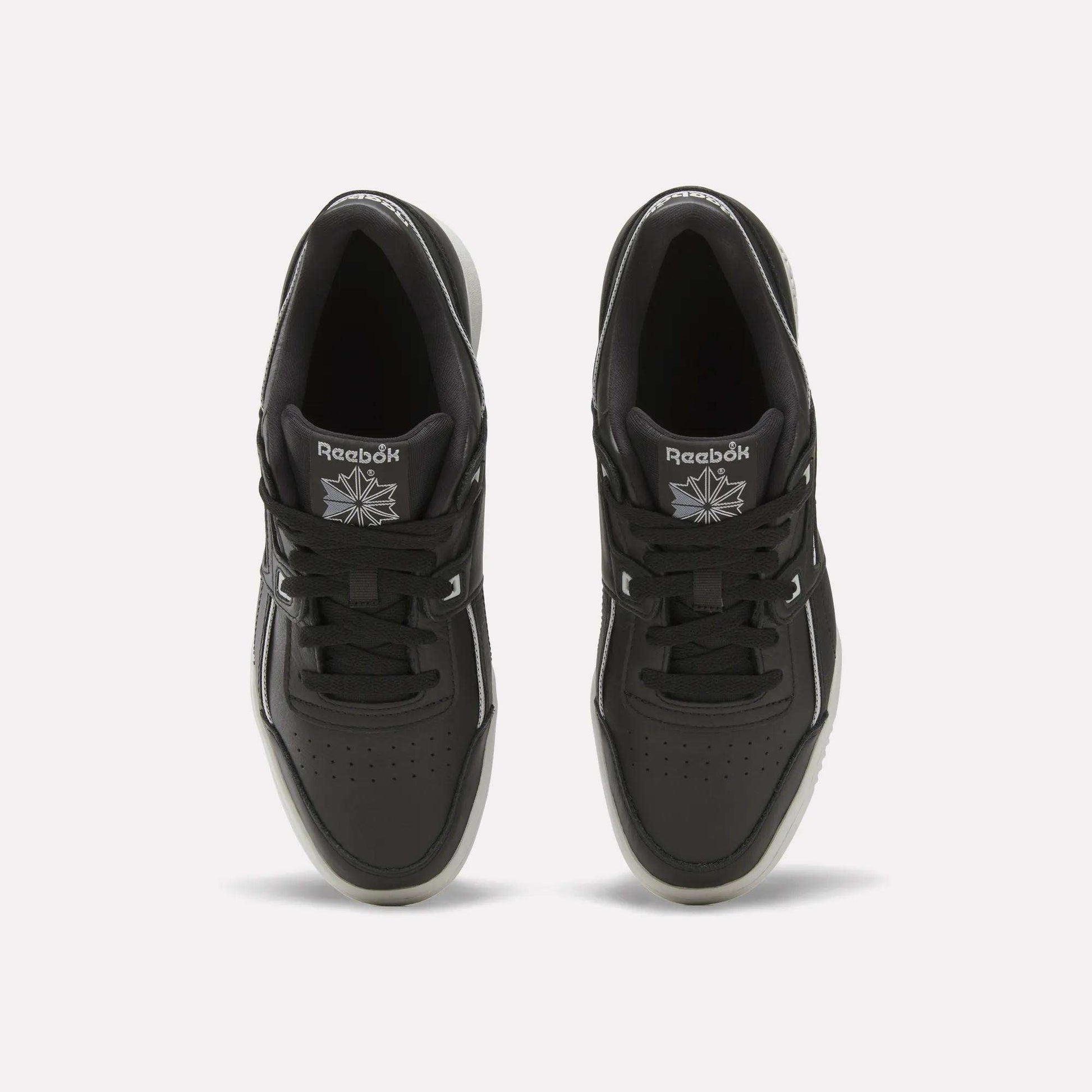 Top view of a pair of black Reebok Workout Plus Shoes with black laces, white accents, and the Reebok logo in white on each tongue. These sneakers are placed side by side on a plain white background.