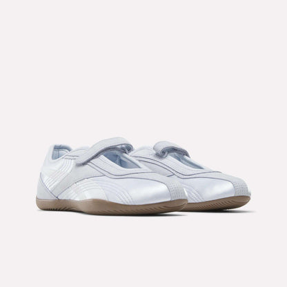A pair of Reebok Women's Ultra Lo Mary Jane Shoes in sleek white with light gray accents, velcro straps, and gum rubber soles, shown on a plain white background.