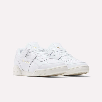 A pair of Reebok Workout Plus Shoes with gold branding, white laces, and off-white soles are displayed on a plain light background, capturing the classic '80s fitness style.
