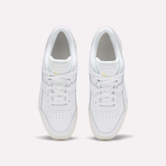 A pair of Reebok Workout Plus Shoes in white, featuring white laces, light yellow accents, perforated toe boxes, and cream outsoles, are seen from above on a plain background for an '80s-inspired look.