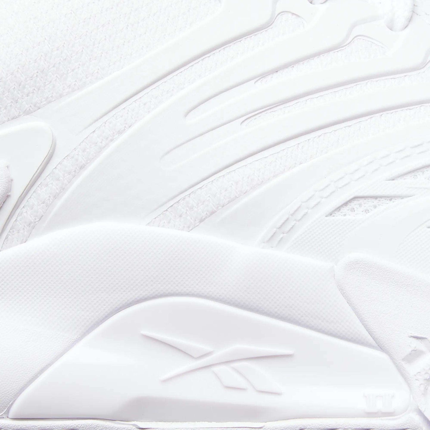 Close-up of a white Reebok Phase EVO Tennis Shoe, showcasing textured, layered materials and the embossed Reebok logo on the side. Smooth curves and raised patterns highlight its durable tennis shoe design.