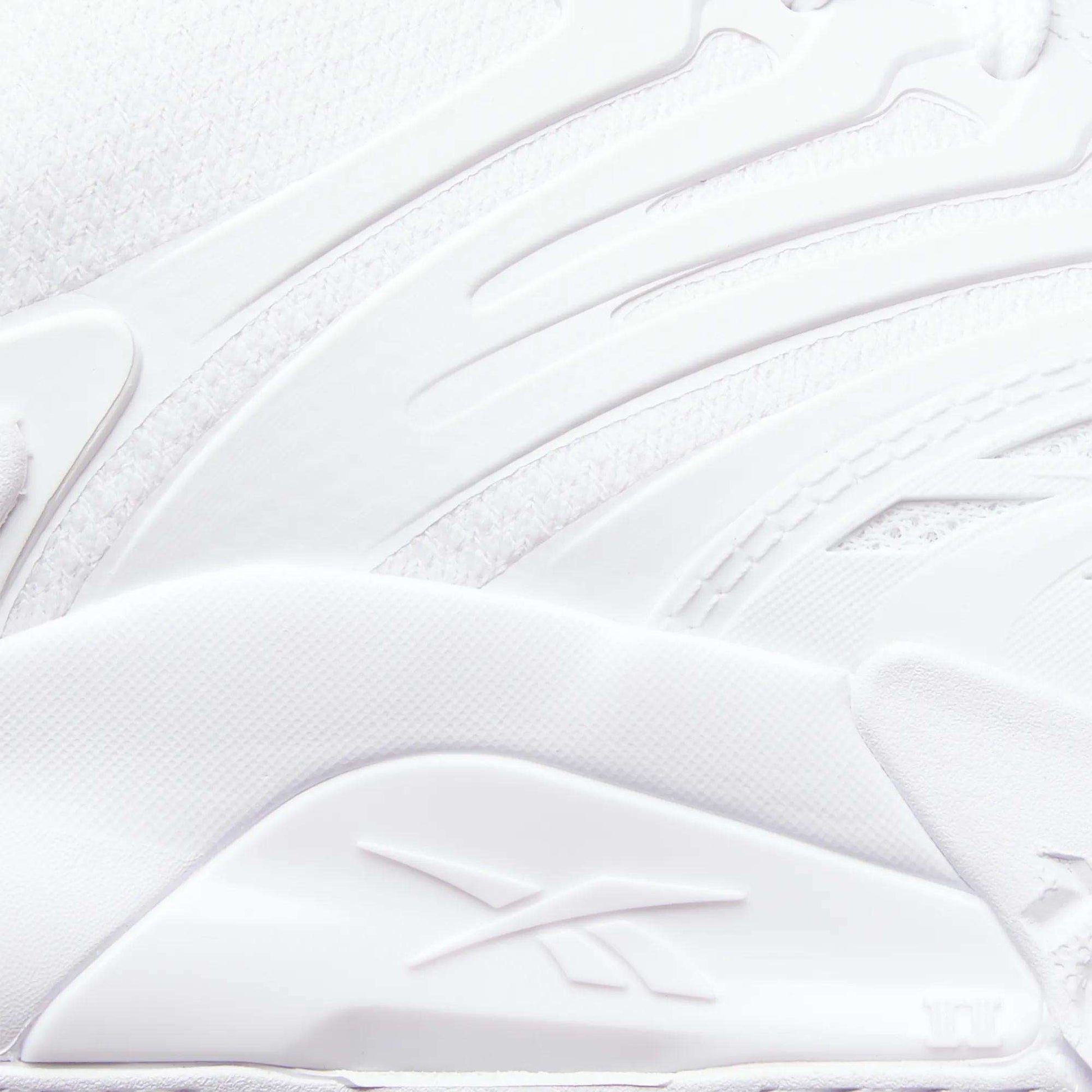 Close-up of a white Reebok Phase EVO Tennis Shoe, showcasing textured, layered materials and the embossed Reebok logo on the side. Smooth curves and raised patterns highlight its durable tennis shoe design.
